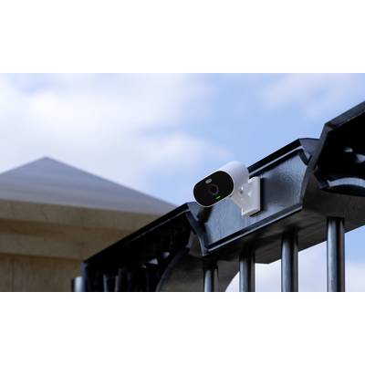 Security camera mounted on a metal fence, monitoring the entrance area of a building under a blue sky.