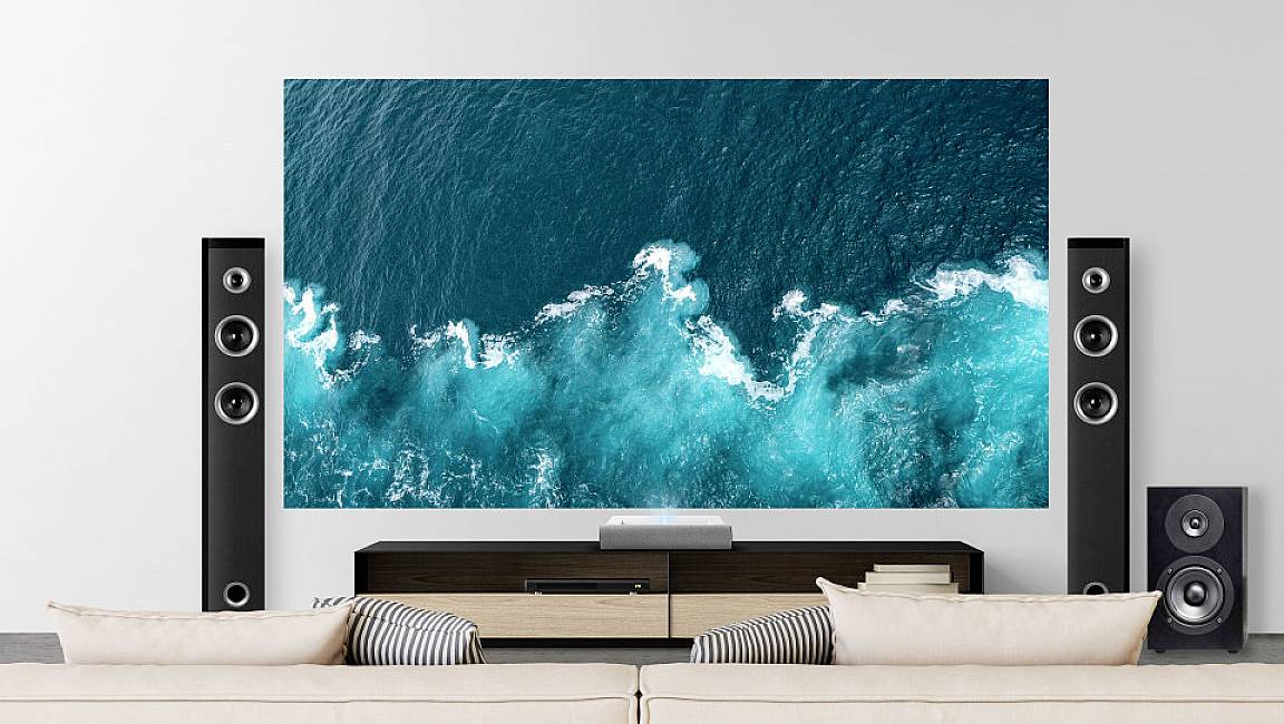 A modern living room with a large television displaying an ocean image. Two speakers are positioned on the left and right.