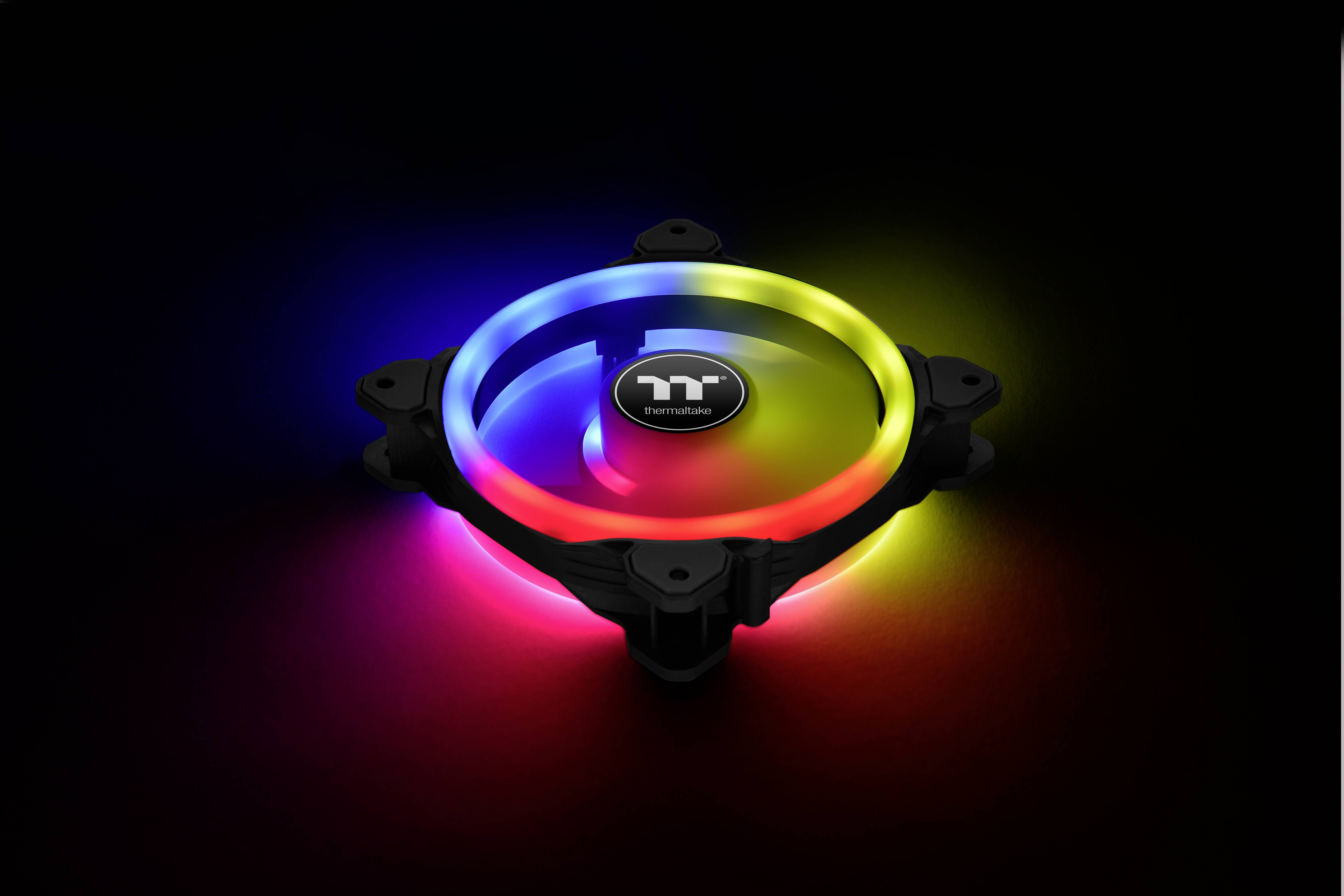 A Thermaltake computer fan with illuminating RGB LEDs in red, yellow, blue and purple, glowing brightly in a dimmed room.