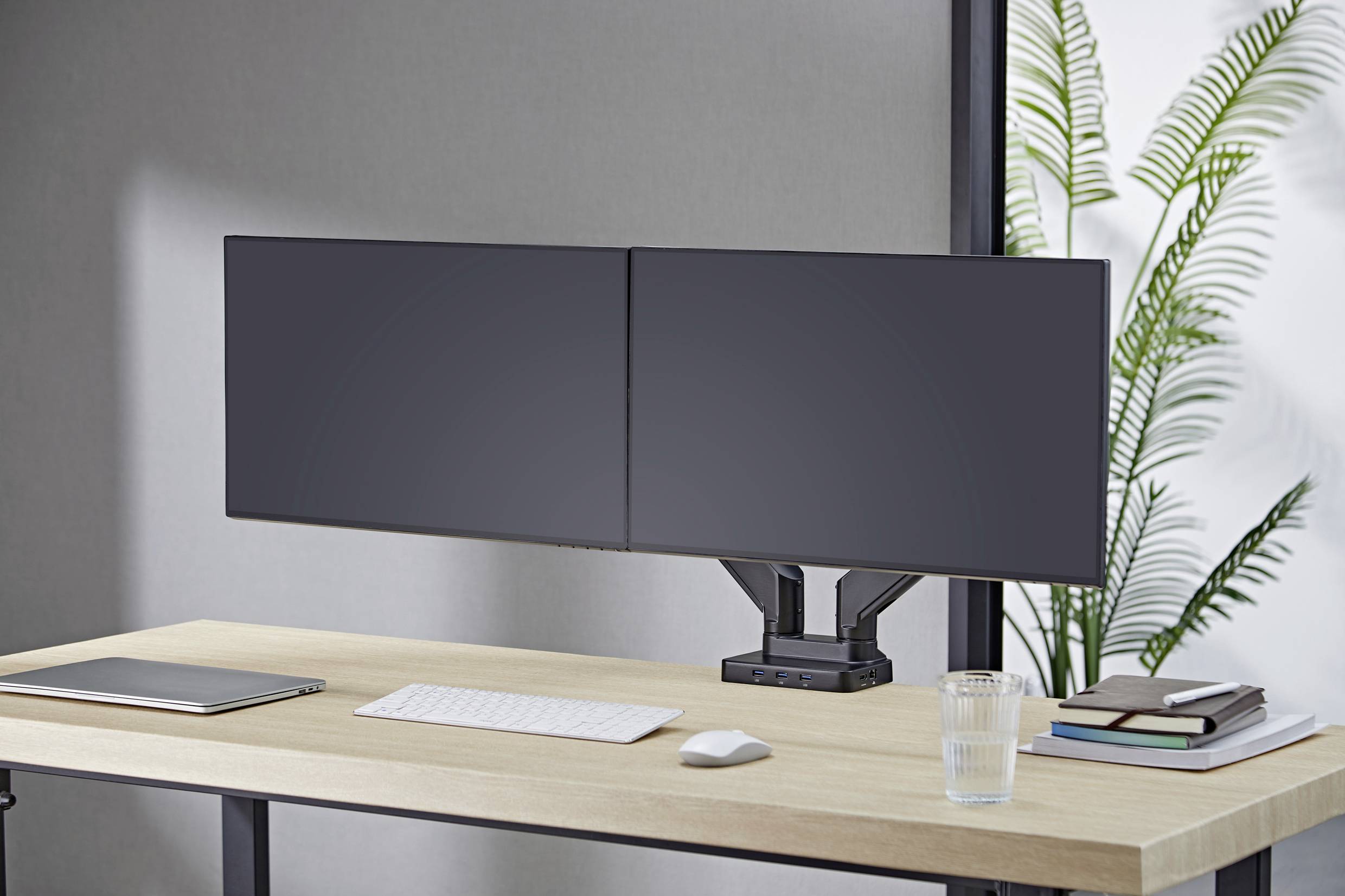 A modern desk with two large computer monitors, a keyboard, a laptop and books. A plant is visible in the background.