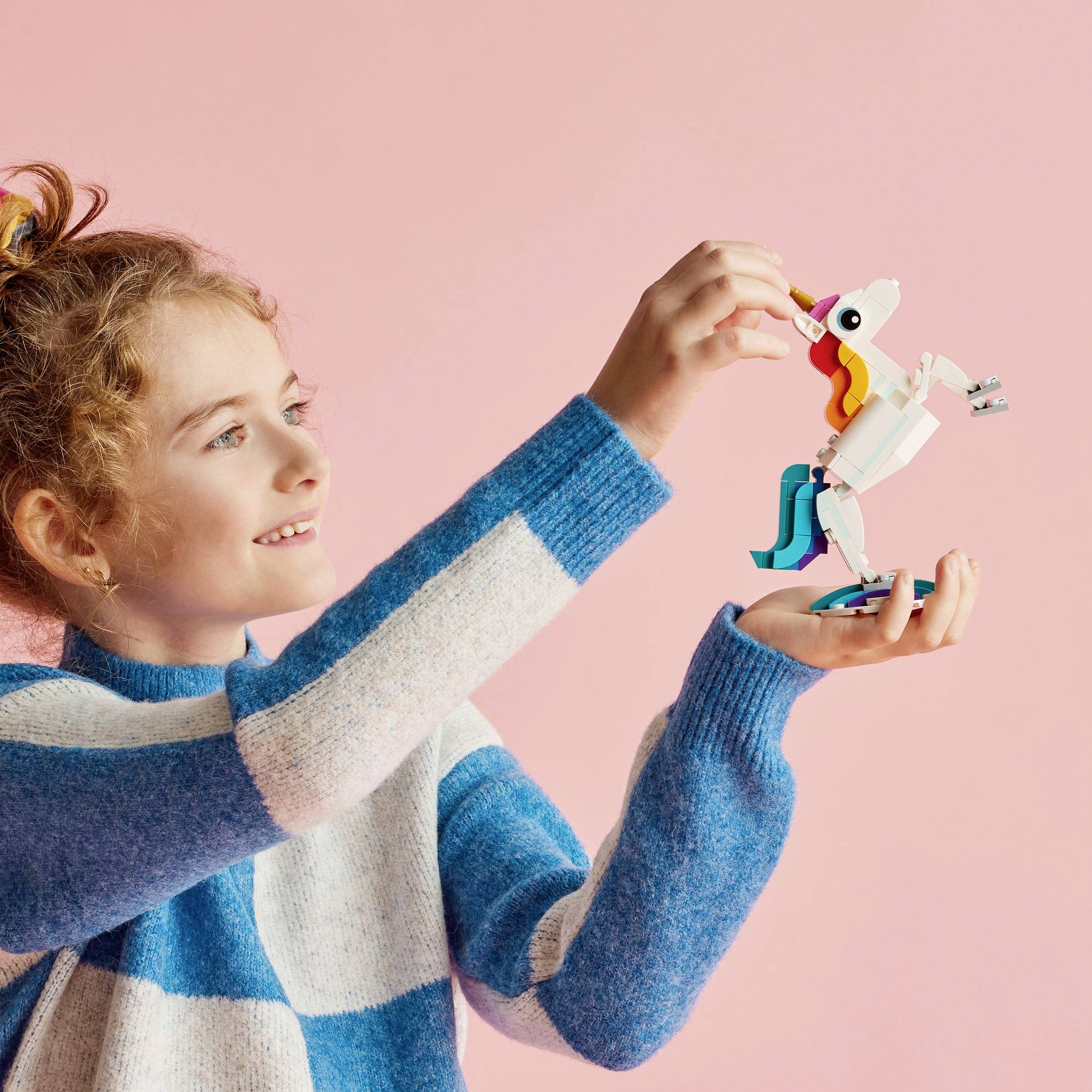 A child is holding a colourful toy unicorn and smiling at it.