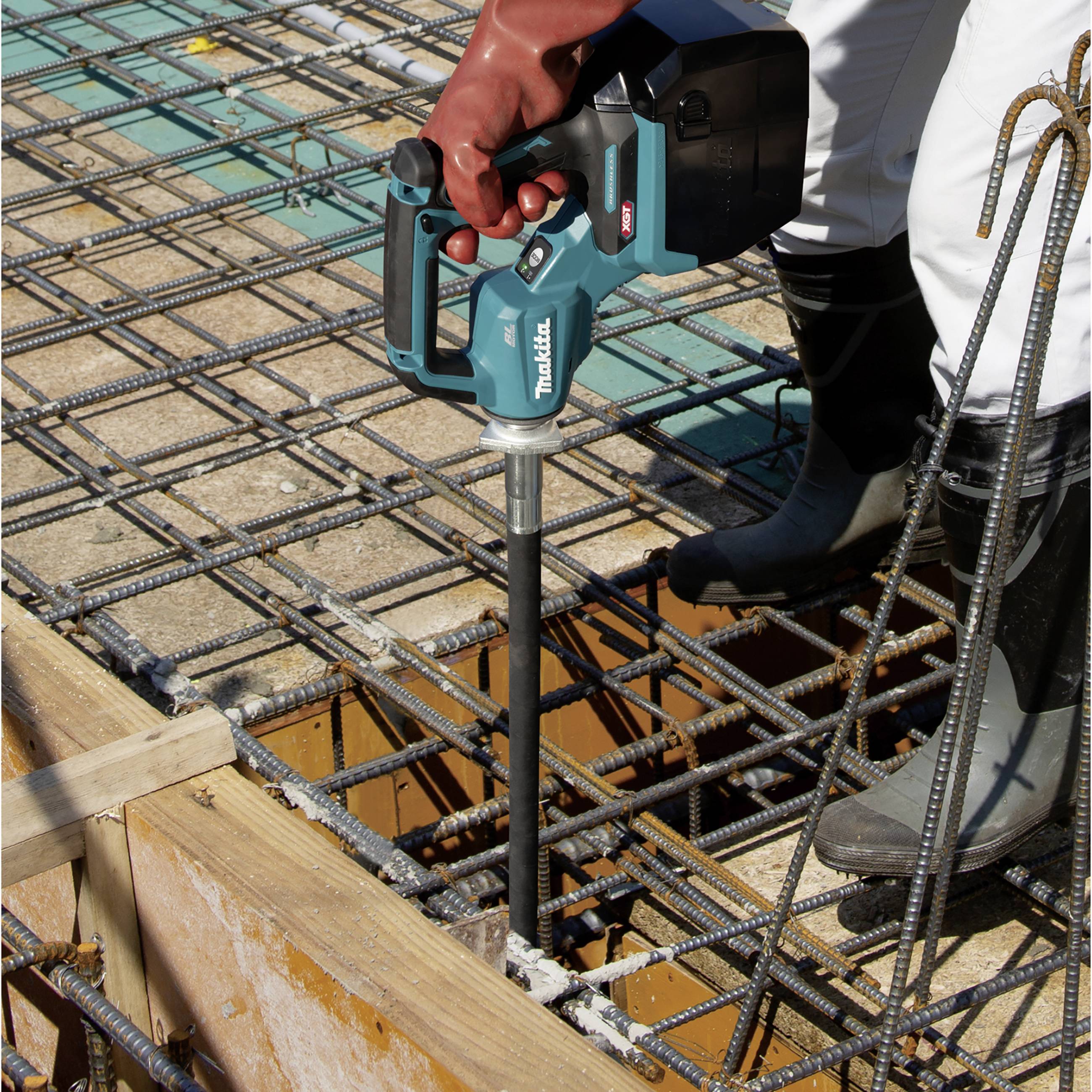 A worker is using an electric tool to compact concrete on a construction site with steel reinforcement.
