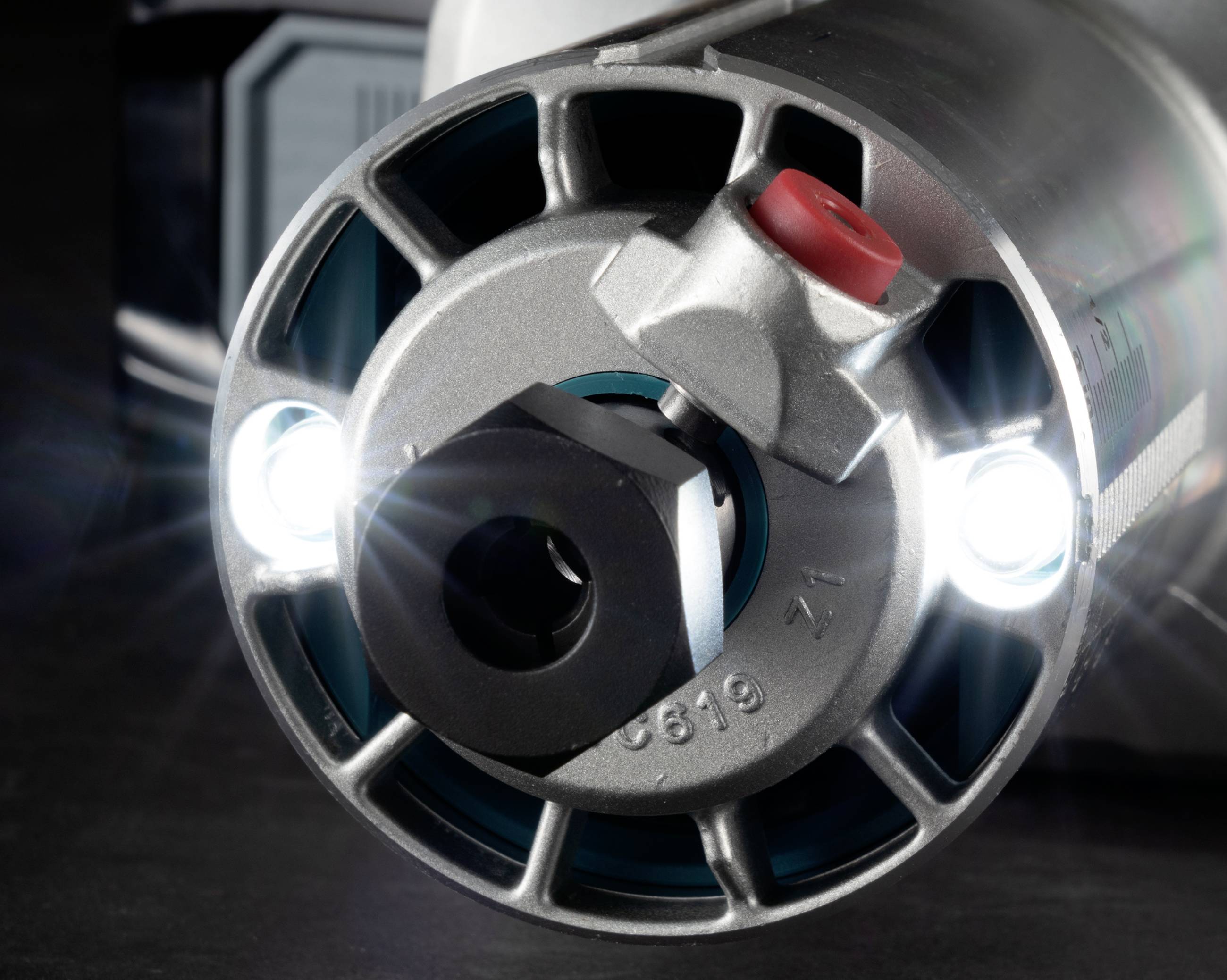 Close-up of a circular machine component with two bright LED lights, a hexagonal insert in the centre, and a red cap on top.