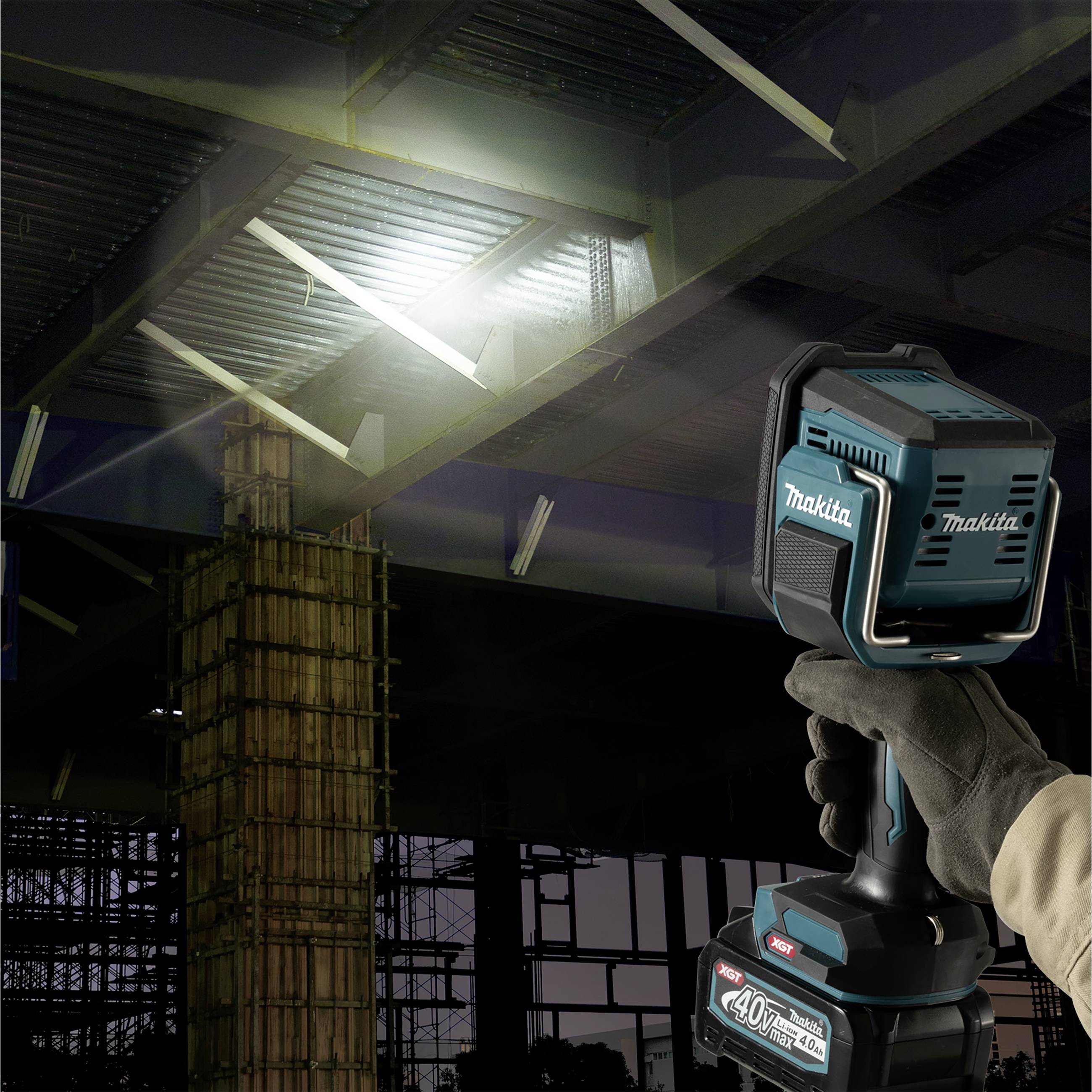 A person is holding a cordless Makita battery-powered torch in a partially lit building shell to illuminate a steel structure.