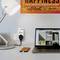 A desk with a lamp, a socket with a charging cable and a smartphone. In the background, a laptop with an image website open.