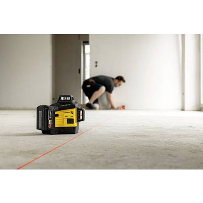 A yellow laser levelling device projects a red line onto the floor. In the background, a person is kneeling and working.