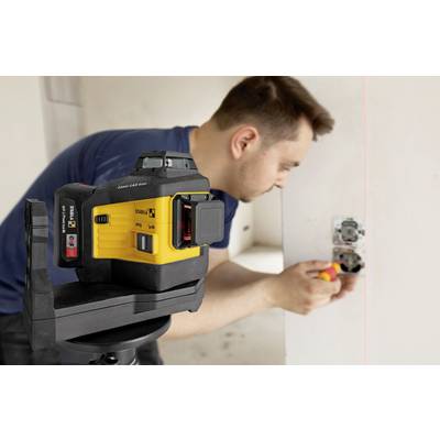 A man is installing a socket in a wall, with a yellow cross-line laser device on a tripod serving to align it.