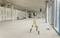 Large empty space in a building under construction, a worker is installing lighting on the ceiling, while a laser level stands on the floor.