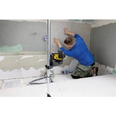 A tradesman in blue workwear is laying tiles in a bathroom using a laser levelling device.