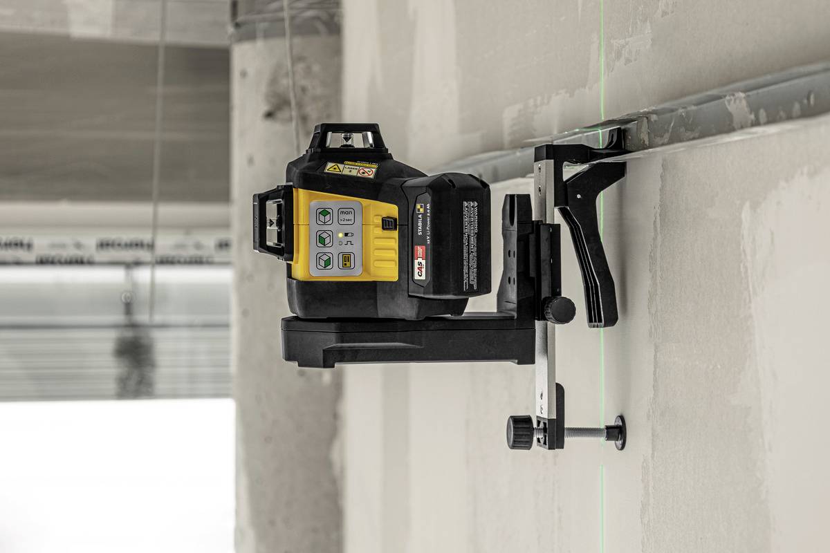 A laser levelling device is mounted on a wall, projecting green laser line signals onto the surface for precise alignment.
