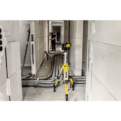 A construction site inside a building with a surveying instrument mounted on a tripod in the foreground. A worker can be seen in the background.