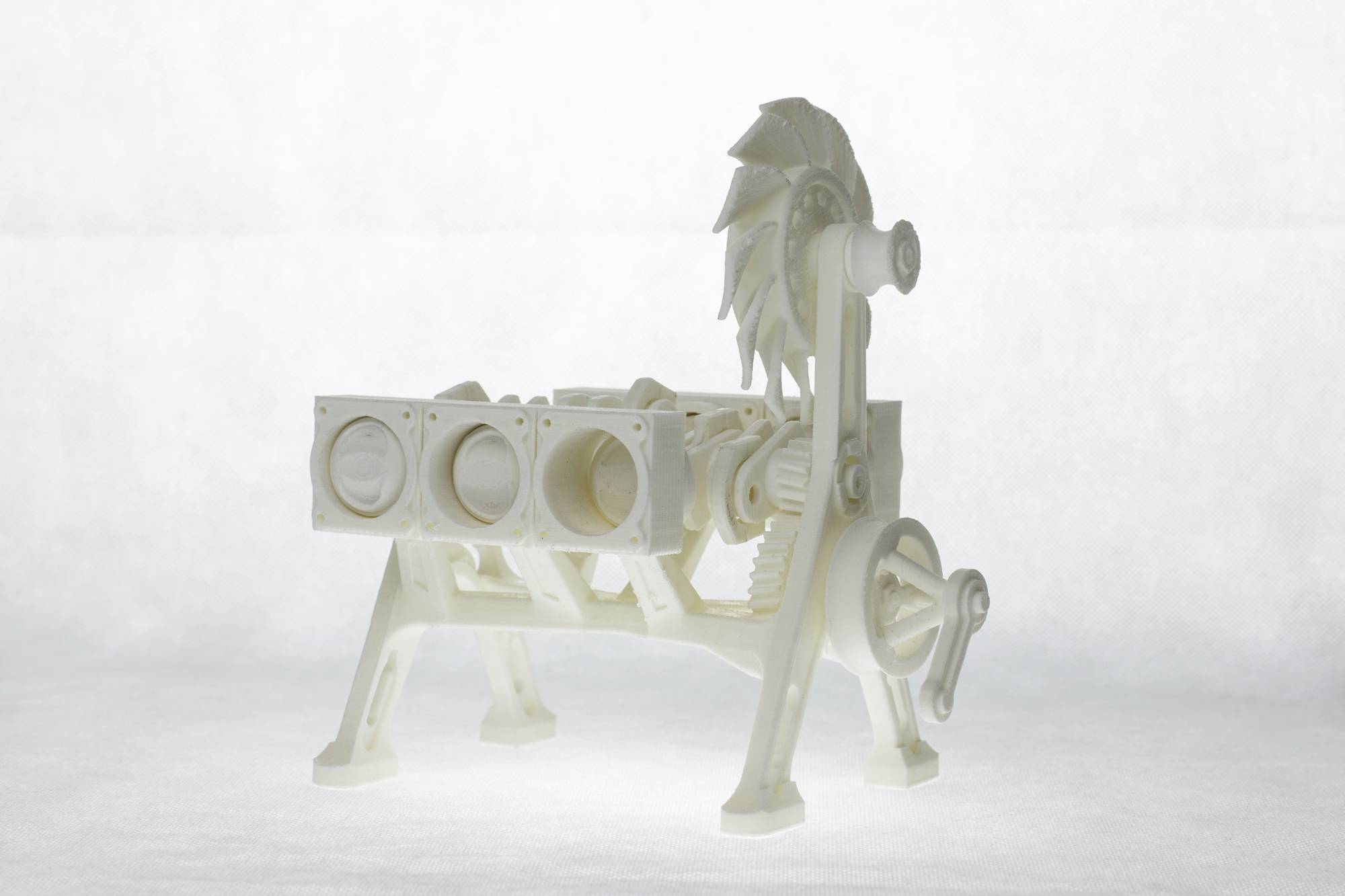 A white plastic model of an engine with visible cylinders, gears, and a fan wheel. The model is positioned on a table.