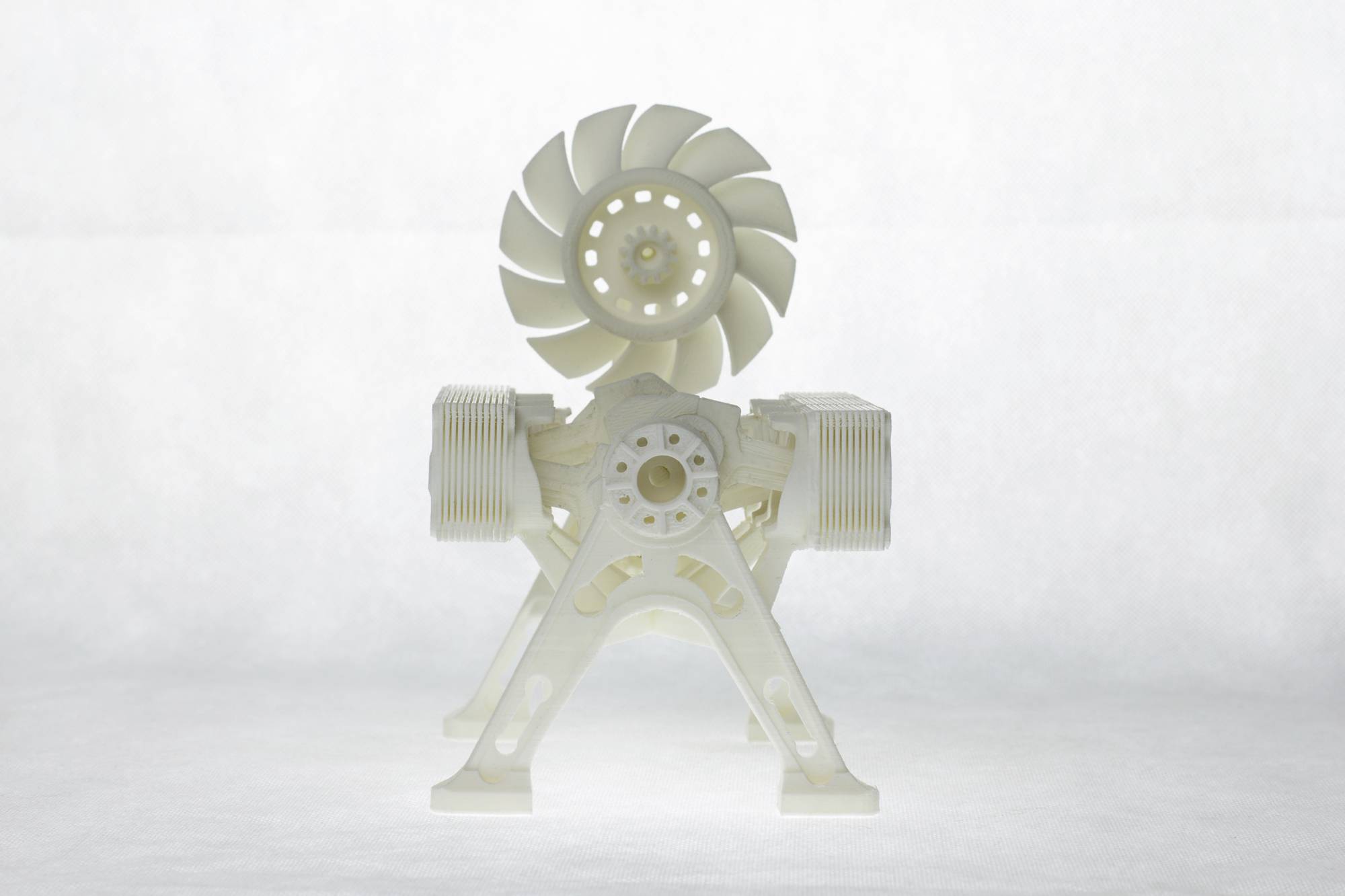 A white mechanical model with gear and propeller structure stands on transparent legs, against a light background.
