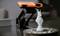 The image shows a white chess knight on a round table with a 3D scanner behind it. The scanner is orange and black.