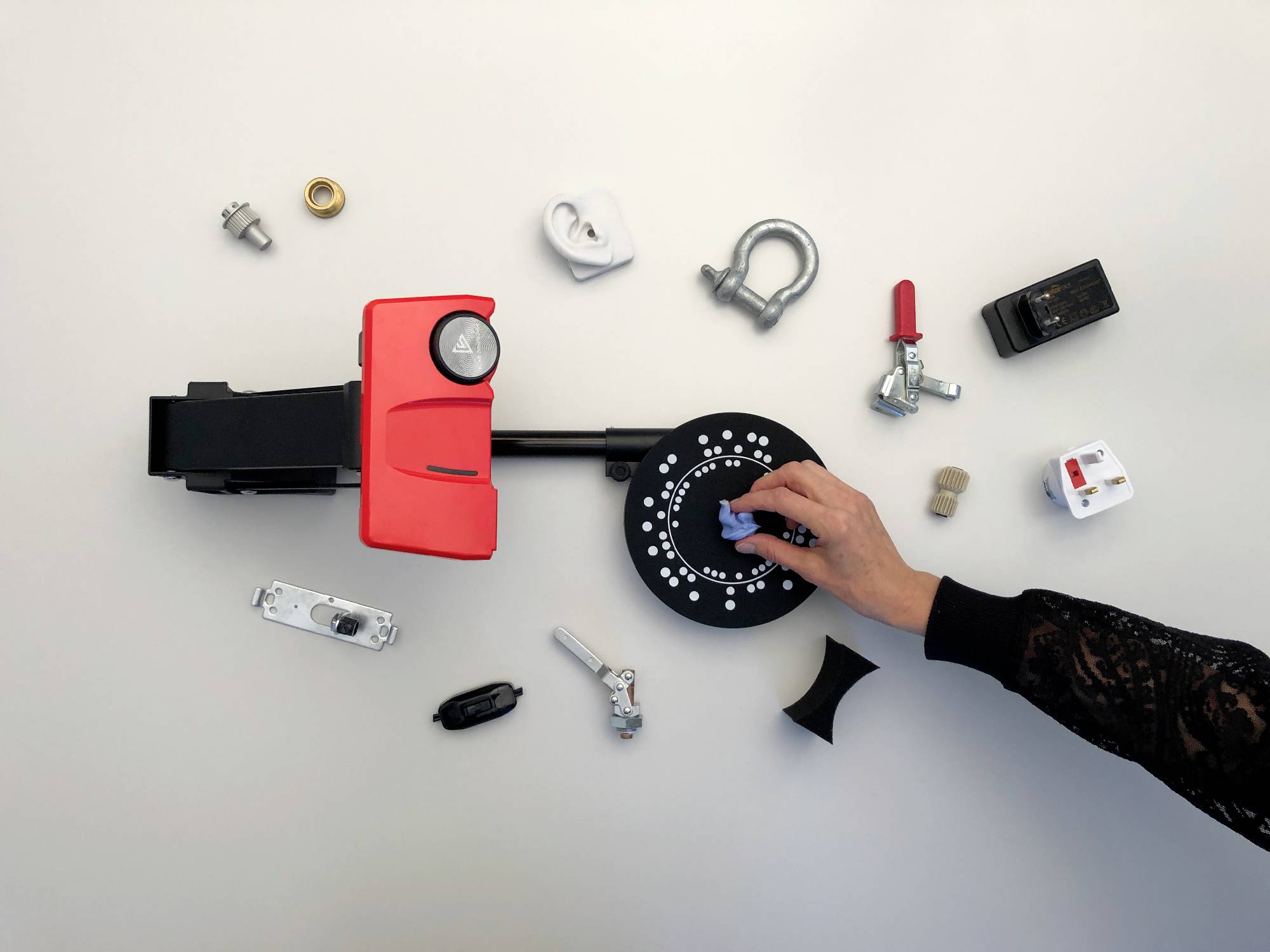 A hand turns the dial of a red safe. Various mechanical and electronic components are scattered around it.