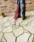 A person is removing weeds from the joints of a paved stone path in front of a brick wall using a red device.