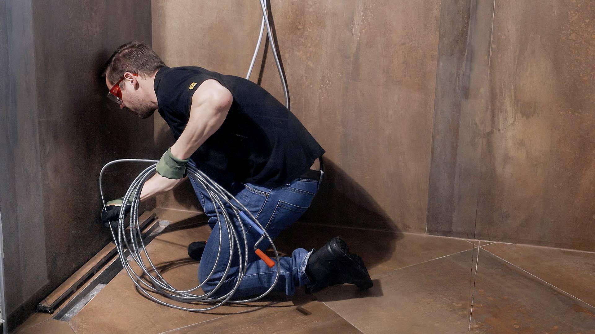 A man in workwear is installing cables in a room with brown walls. He is kneeling while laying cables in a corner.