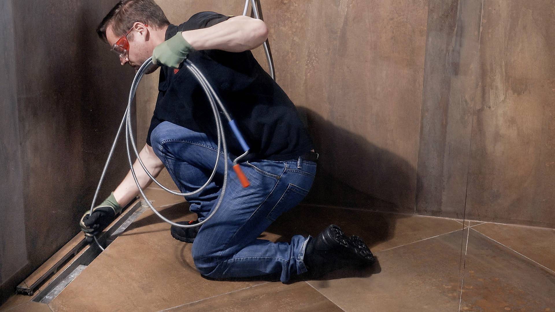A man in work attire is kneeling and installing cables in a room with brown walls.