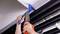 A person is installing a blue water pipe on the ceiling using a modern crimping tool. Pipes run parallel along the ceiling.