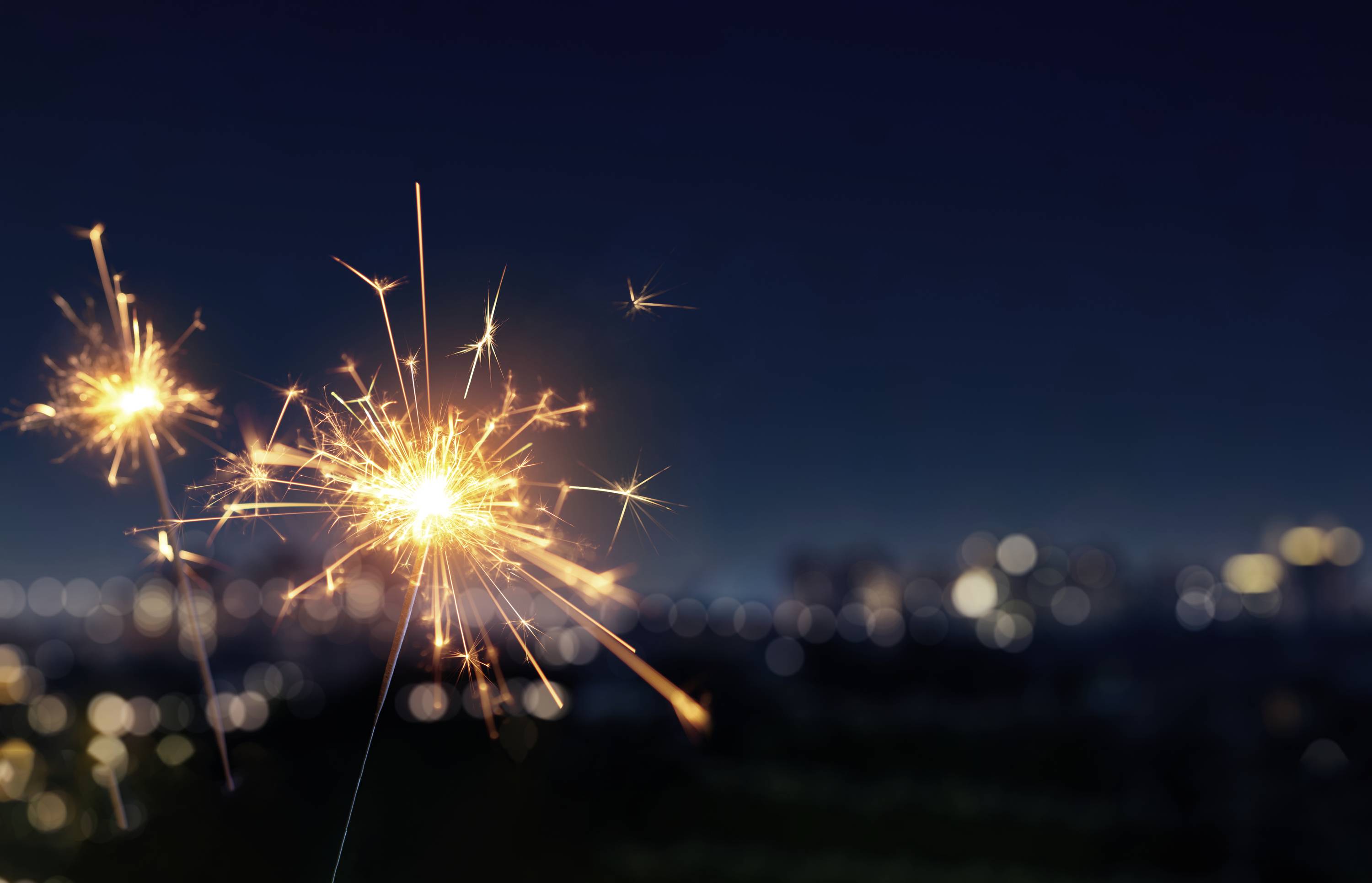 Sparkling sparklers in front of a nighttime city skyline, blurred in the background, creating a festive atmosphere.