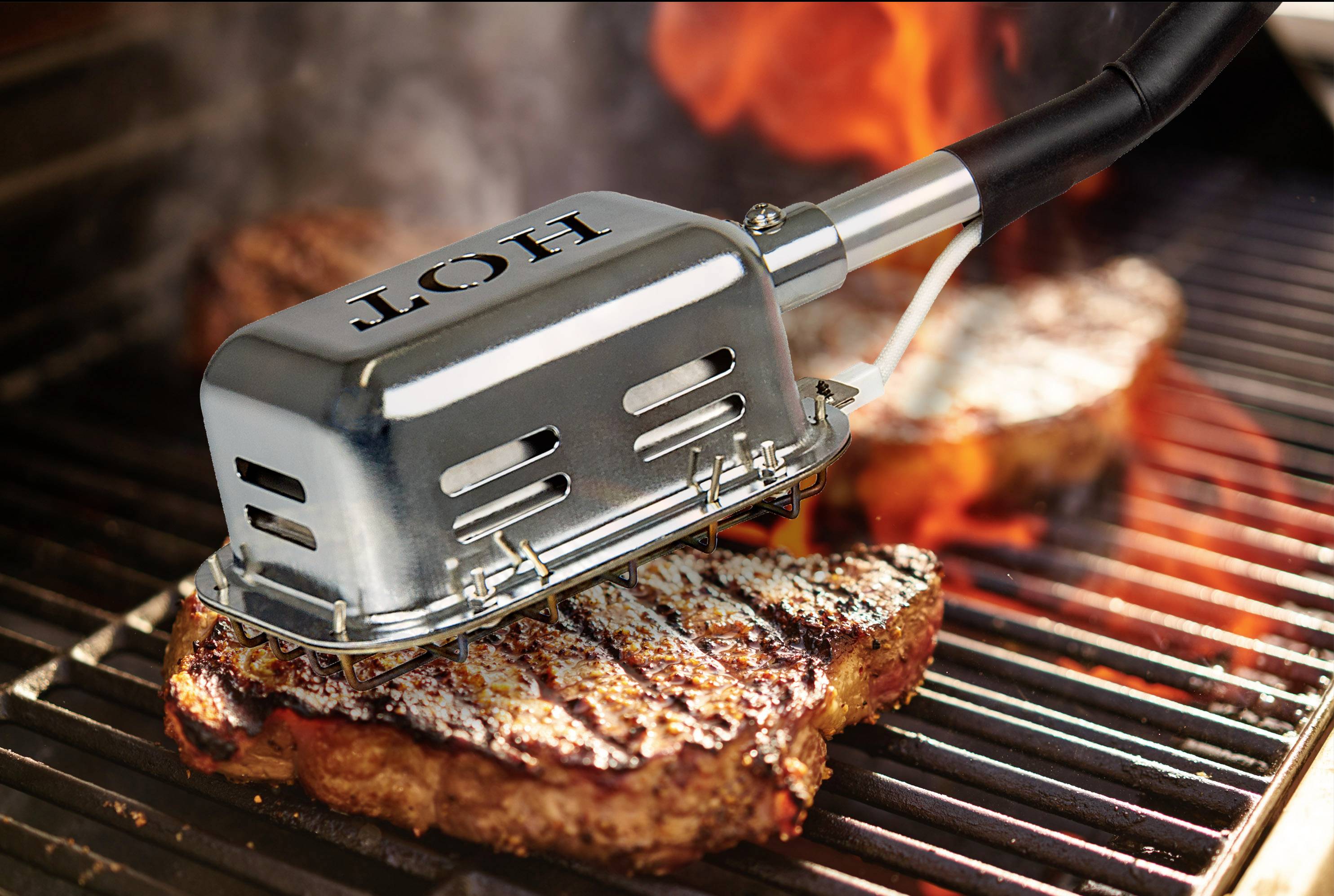 A steak is being marked on a grill with a branding iron that has imprinted 'HOT'. Flames are visible in the background.
