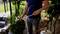 A man is holding a weed burner with a gas canister in the garden. He is standing on a path next to green plants and a fence.