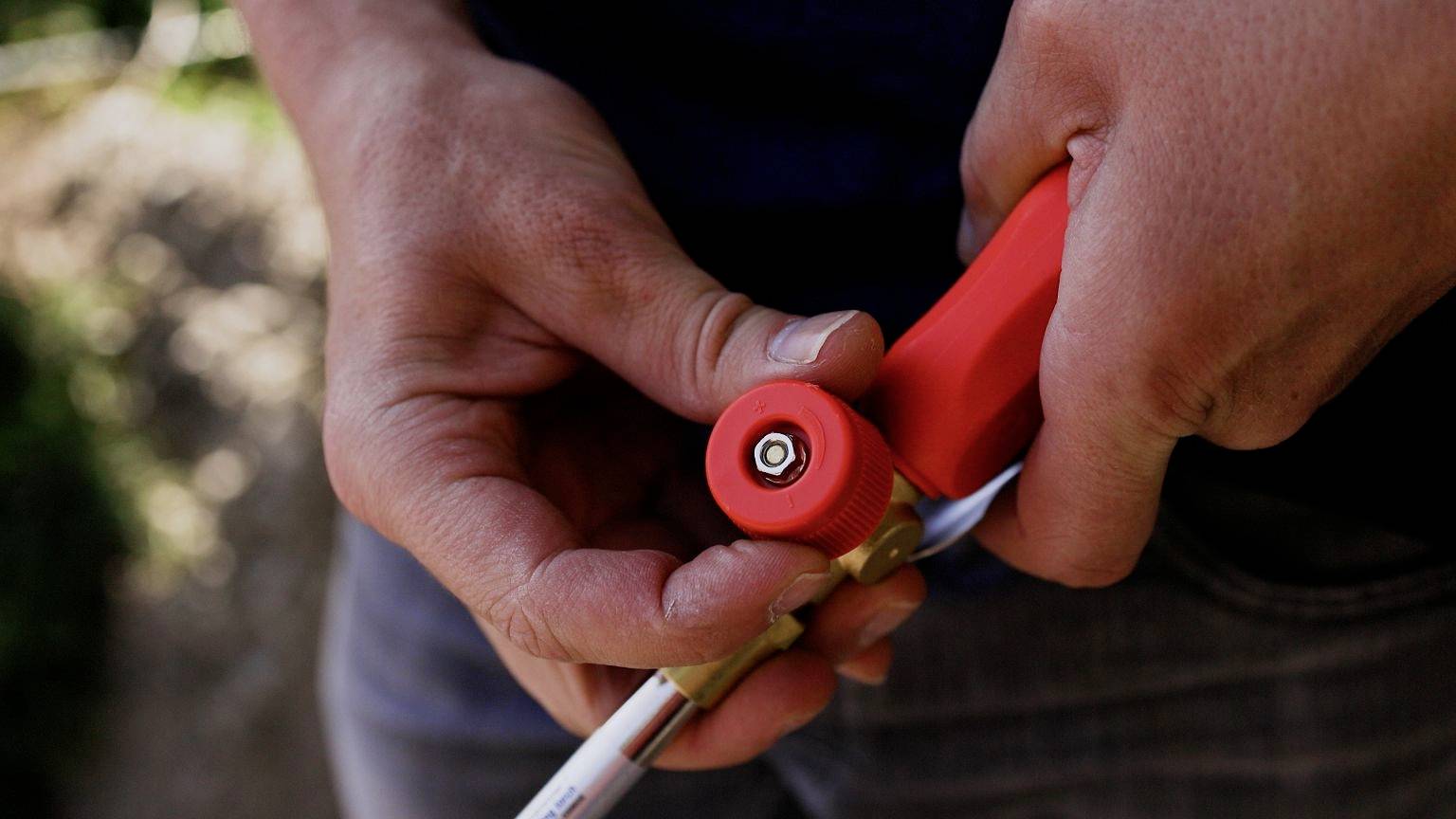 A person is holding a red handle with a tool, concentrating intently on precision work outdoors.