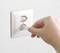 A hand is inserting a white plug into a white socket on a white wall.