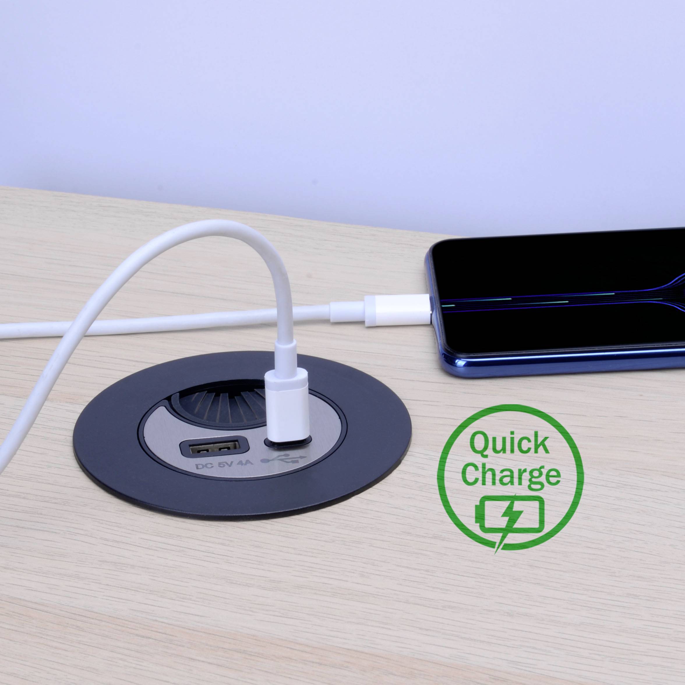 A smartphone is charging wirelessly on a table next to a quick-charge station. A charger is connected to the station.