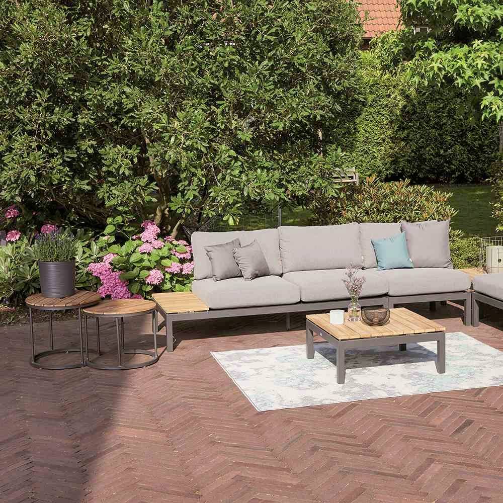 Garden with a grey sofa set, wooden table, plants in the background and paved flooring, perfect for outdoor relaxation.