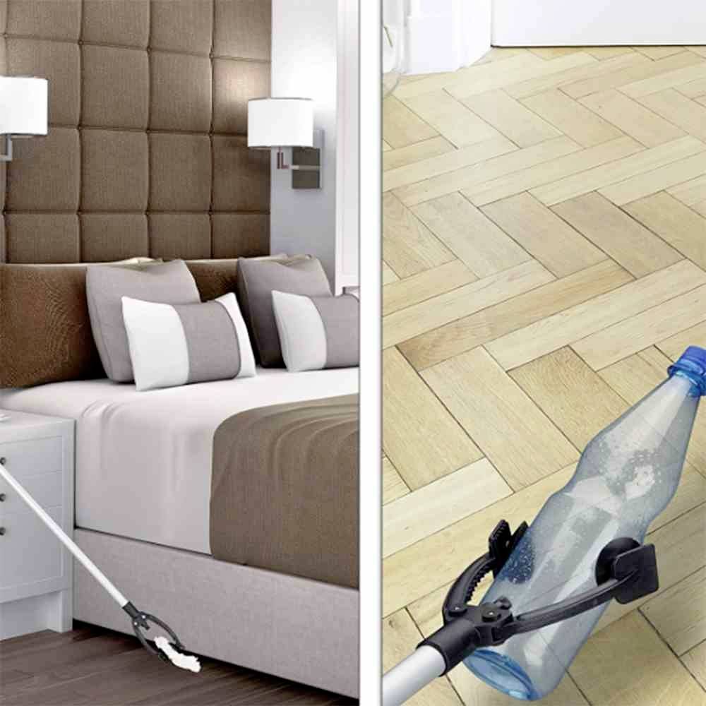 A robotic arm picks up a plastic bottle from the wooden floor. Bedroom with a double bed and beige bedding in the background.