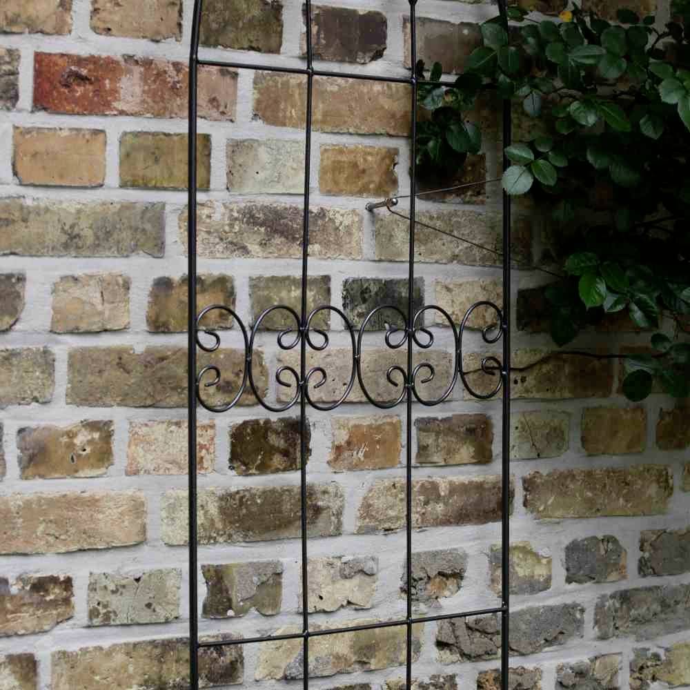 An wrought-iron grating leans against a brick wall. A rose branch winds its way through the lattice.