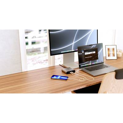 Workplace with a laptop and smartphone, both connected to a charging device. A monitor displays abstract lines on a black background.