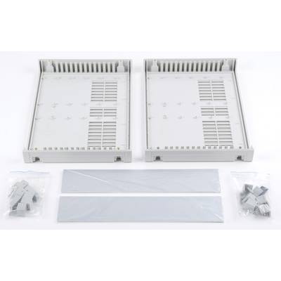 Two grey, rectangular plastic casings with ventilation slots lie open. Beside them are two narrow covers and small clips in plastic bags.
