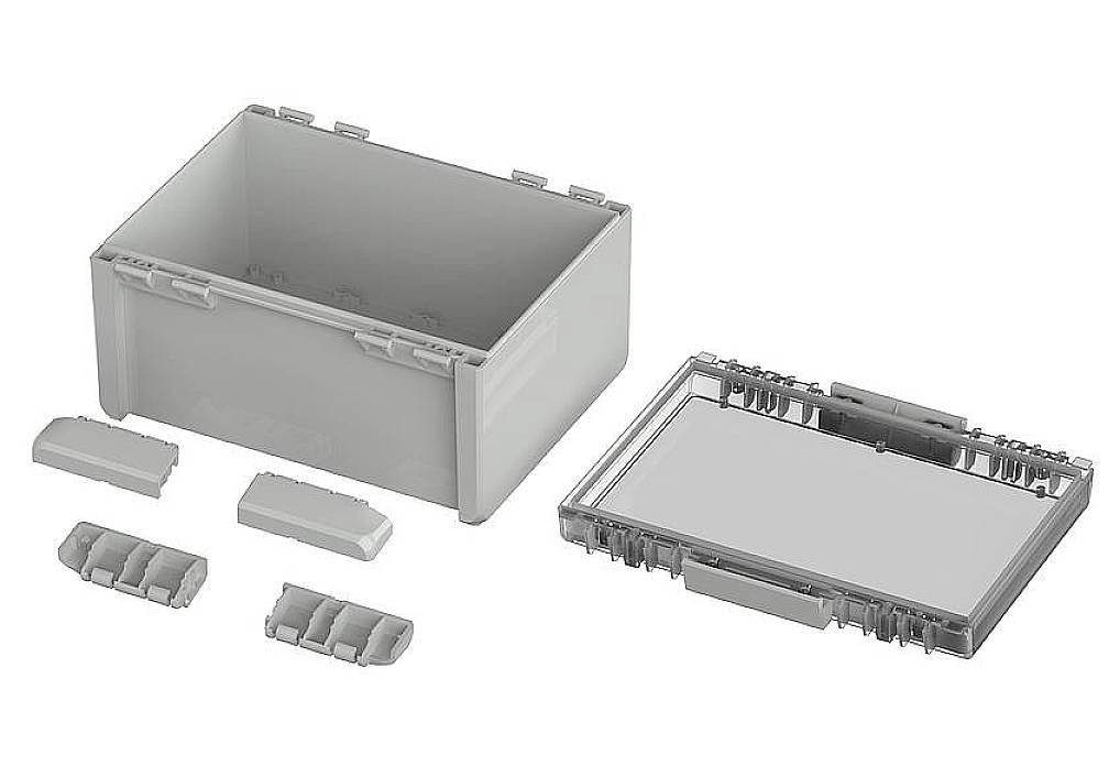 A rectangular, grey plastic enclosure with an open lid lies next to a transparent cover and insertion modules.