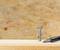 'A screwdriver is lying beside a screw standing vertically on a wooden surface, against a plywood background.'