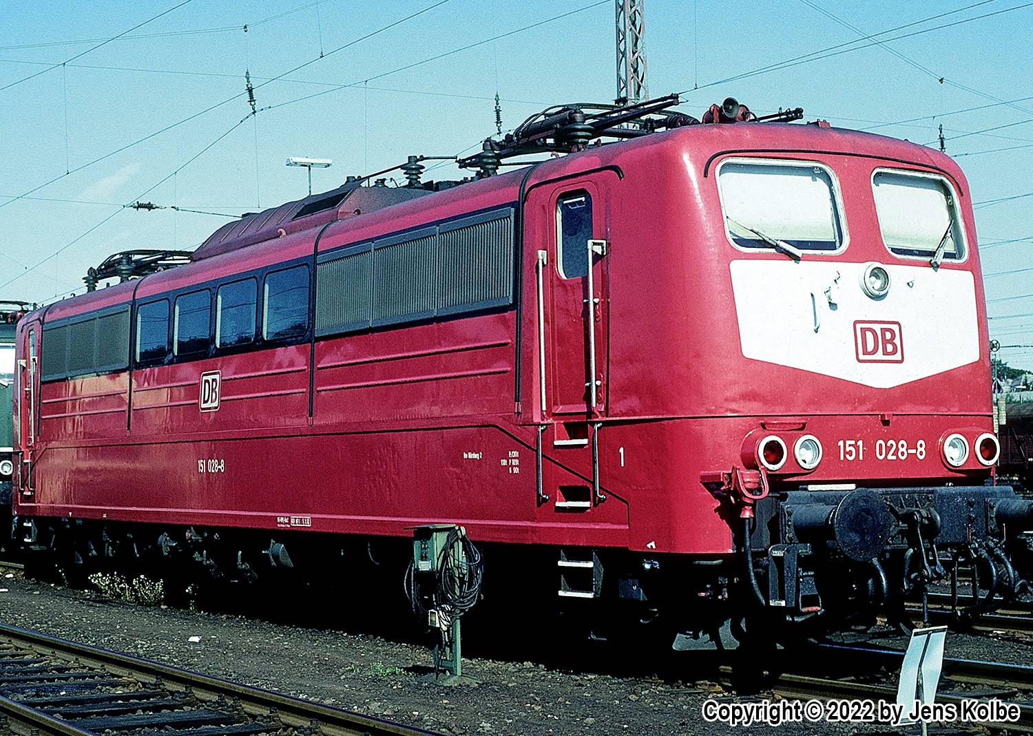 A red electric locomotive from Deutsche Bahn is standing on a siding outdoors.