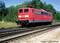 Red train of Deutsche Bahn on a railway track in a rural setting on a sunny day. Trees in the background.
