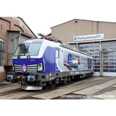 A blue electric train stands on tracks in front of a railway depot building belonging to Railsystems RP Ltd.