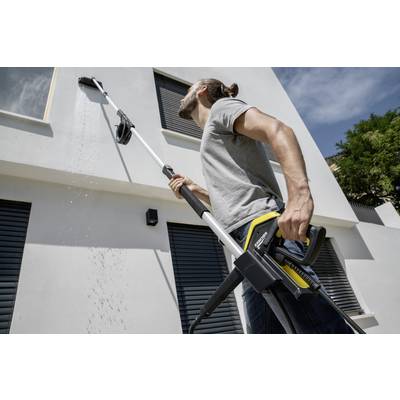 A person is using a pressure washer to clean high windows on a residential house. The cleaner is spraying water onto the window.