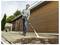 A person power washes an outdoor patio, cleaning away dirt. They're using a yellow pressure washer connected to a water hose.