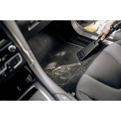 A person is hoovering the floor of a car to remove scattered dirt. The vacuum cleaner has a narrow nozzle for precise cleaning.