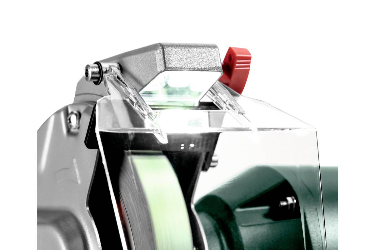 A grinding machine with a protective cover and a switched-on lamp. A red button for adjustment is visible.