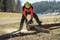 A person is cutting a felled tree trunk with a chainsaw in a rural, woodland setting.