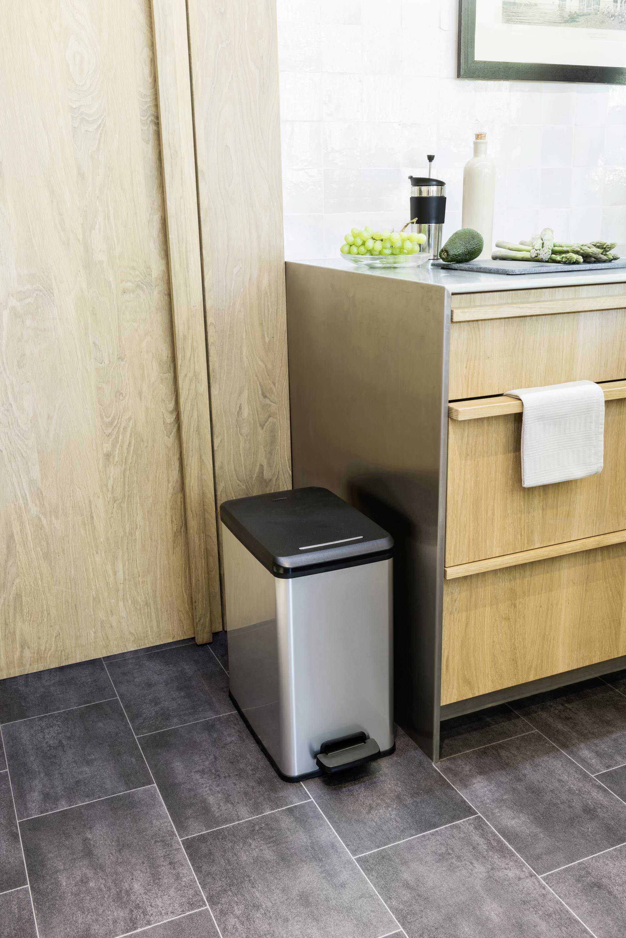 Waste bin in a modern kitchen next to a wooden cupboard, with fruit on the worktop.
