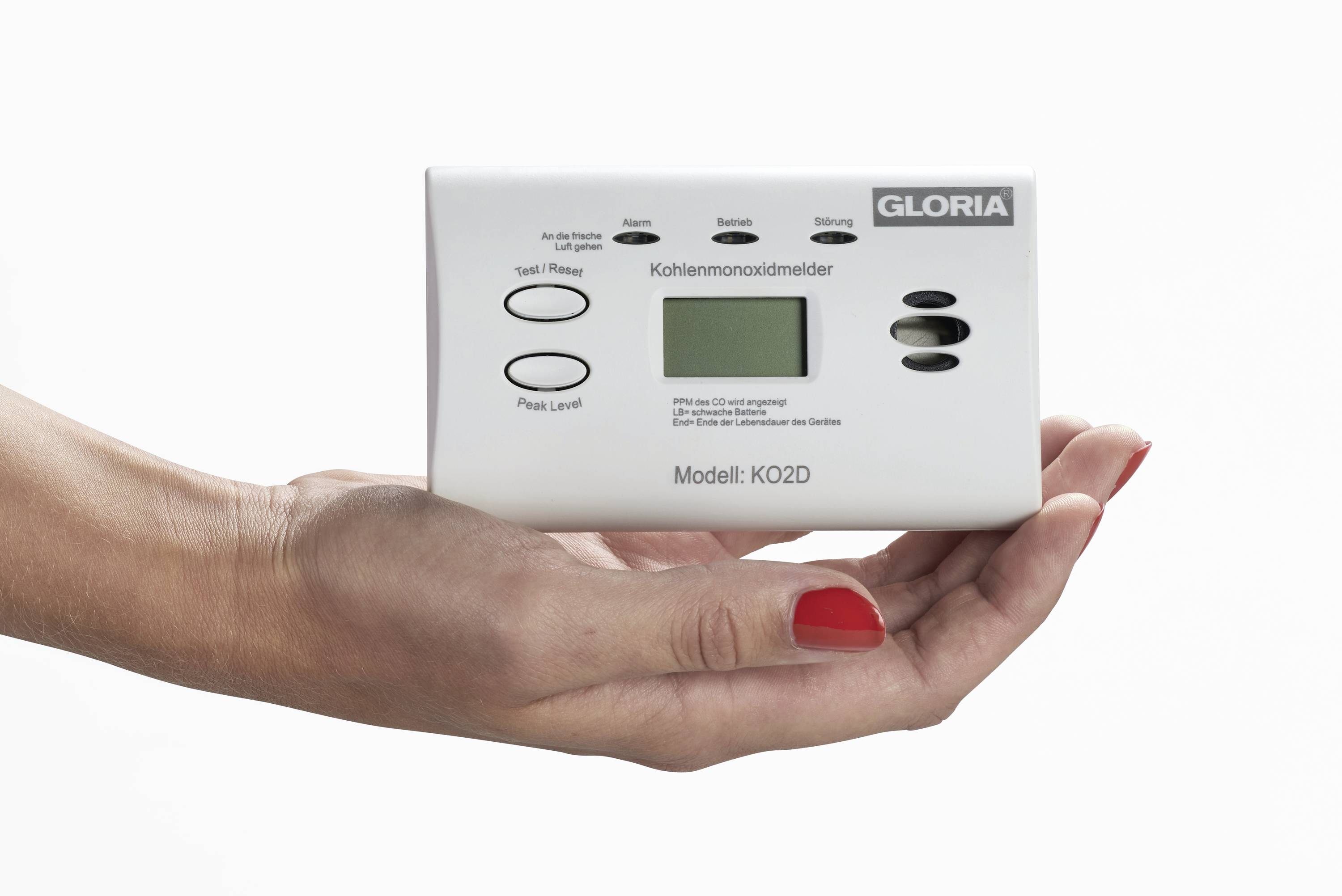 A hand is holding a carbon monoxide detector with a display, model KO2D by GLORIA.