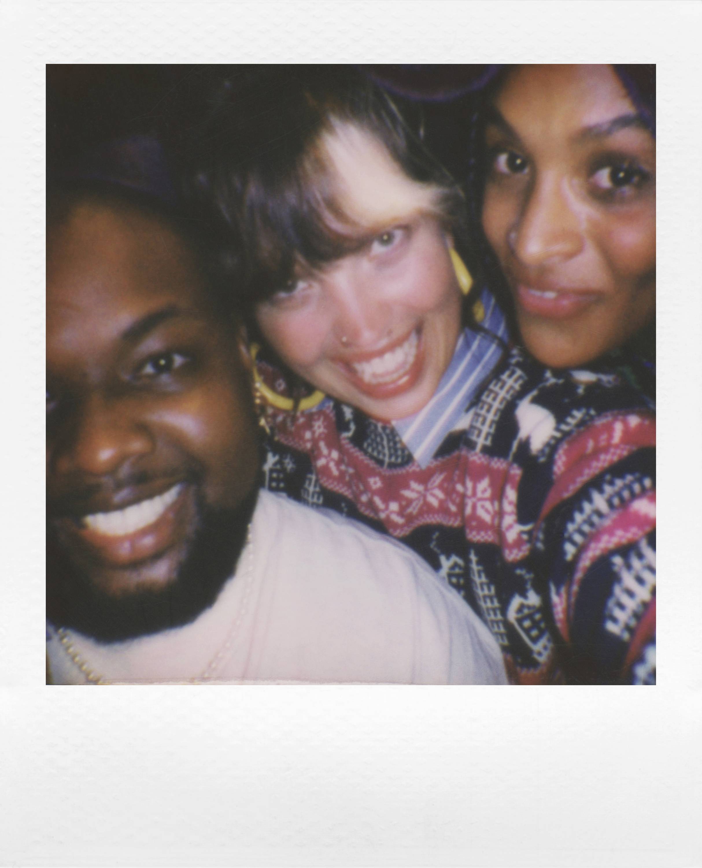 Three people cheerfully pose for a selfie, smiling at the camera. The lighting appears warm and vibrant.