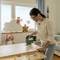 A woman is working on a woodworking project with a jigsaw on a table in a children's bedroom decorated with toys.