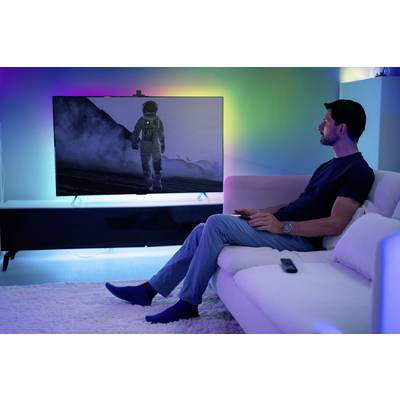 A man is sitting on a sofa watching a film on a large screen that depicts an astronaut in a lunar landscape.