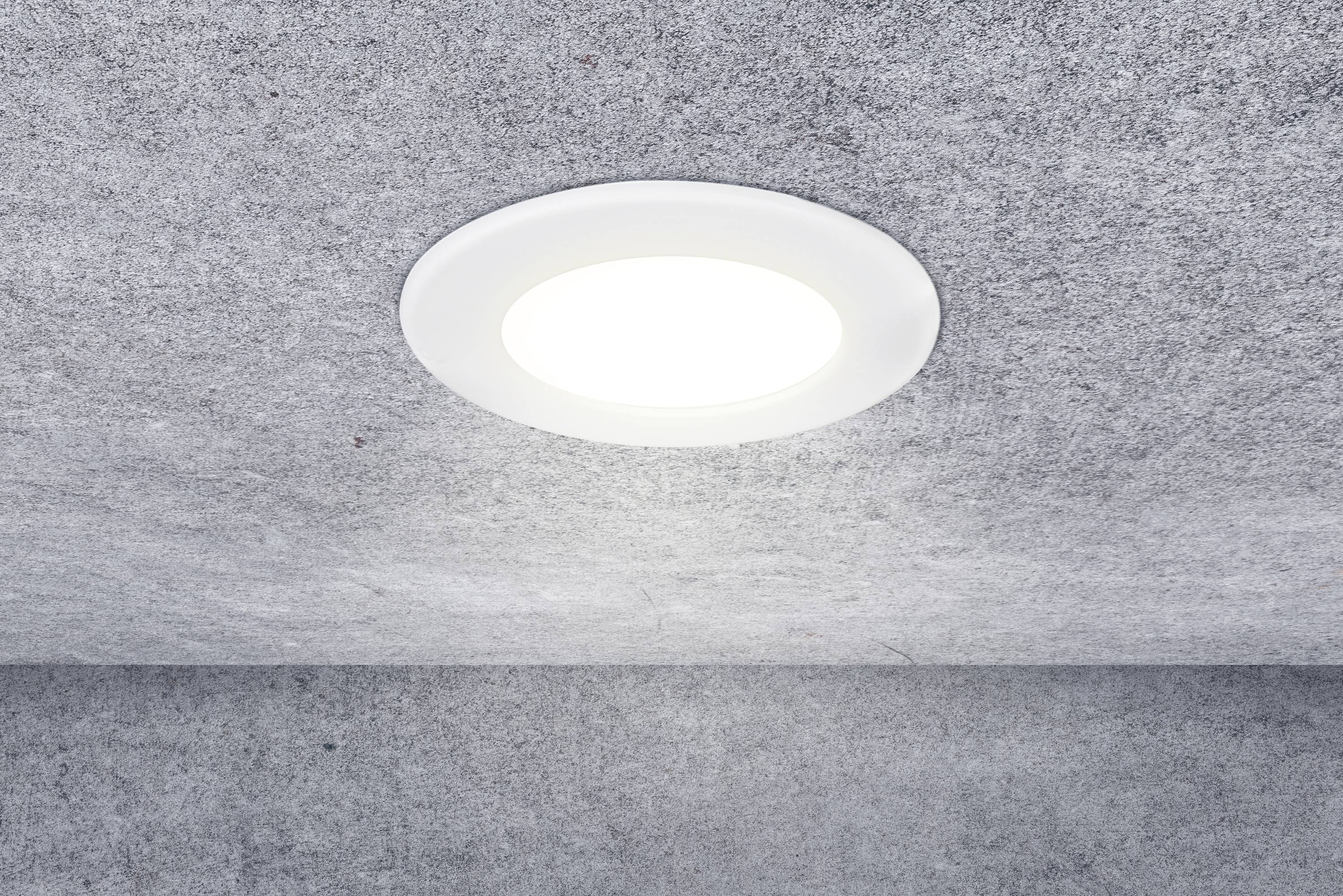 A round, white LED ceiling light shines brightly against a grey ceiling.